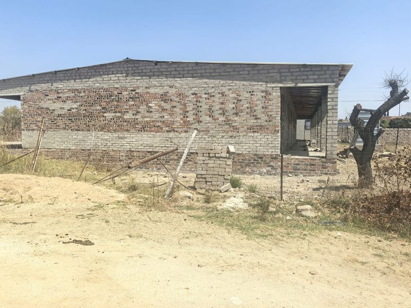 An unfinished residential structure showing exposed brickwork and a metal roof, currently in the early stages of construction.