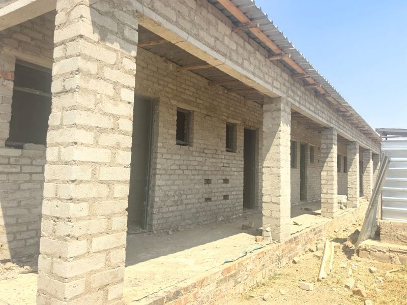 An exterior view of an unfinished apartment building structure featuring exposed brickwork, concrete pillars, and a corrugated metal roof.