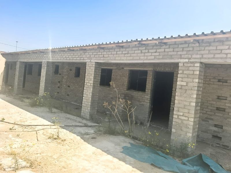 Exterior view of an unfinished apartment block featuring exposed brick walls, concrete pillars, and corrugated roof sheeting in a development phase.