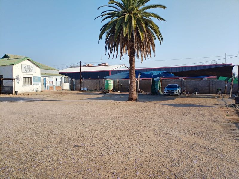 A spacious commercial vacant land lot featuring a gravel yard, perimeter brick walling, and an existing shade cloth structure.
