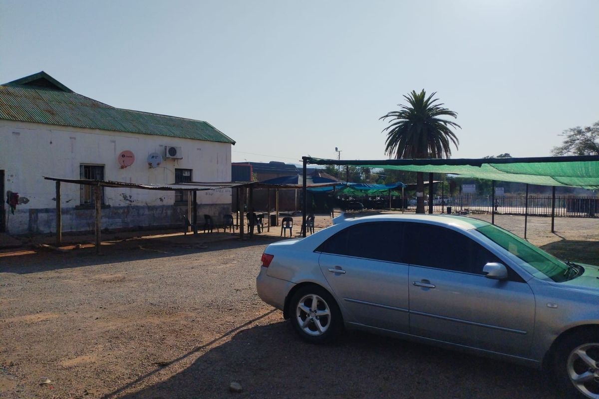 Exterior view of a commercial property featuring a building with a corrugated roof, shade structures, and a gravel parking area.