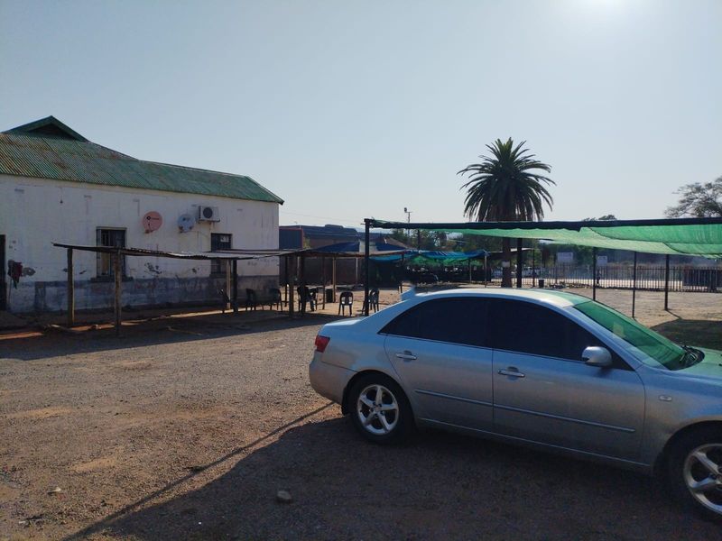 Exterior view of a commercial property featuring a building with a corrugated roof, shade structures, and a gravel parking area.