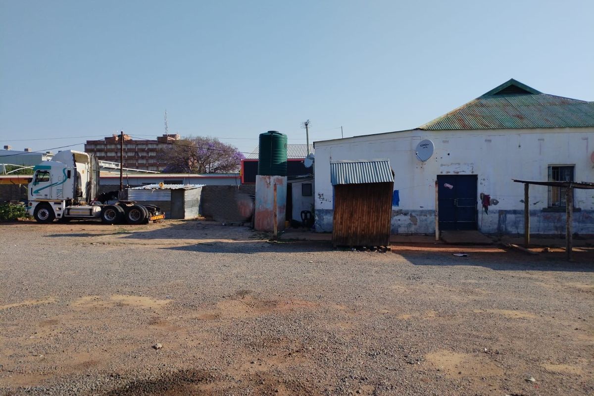 Exterior view of a commercial property featuring a gravel yard, water storage tank, and a building with a corrugated metal roof.