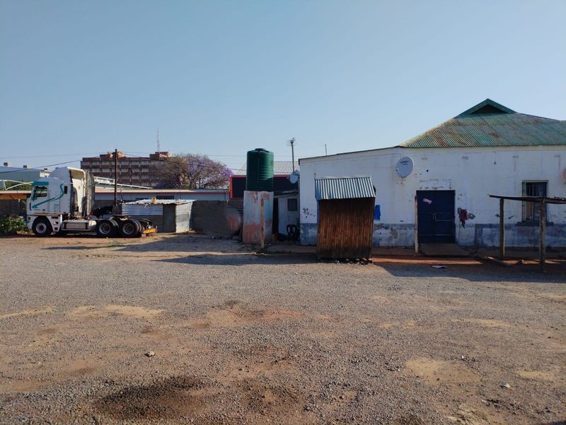 Exterior view of a commercial property featuring a gravel yard, water storage tank, and a building with a corrugated metal roof.