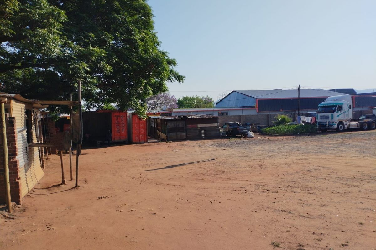A view of a commercial vacant land plot featuring unpaved ground, perimeter walling, and several makeshift shipping container structures.
