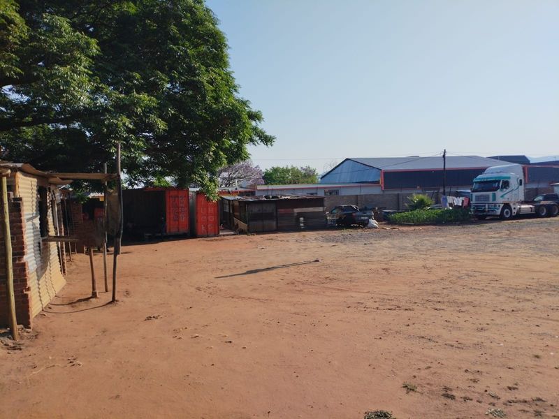A view of a commercial vacant land plot featuring unpaved ground, perimeter walling, and several makeshift shipping container structures.