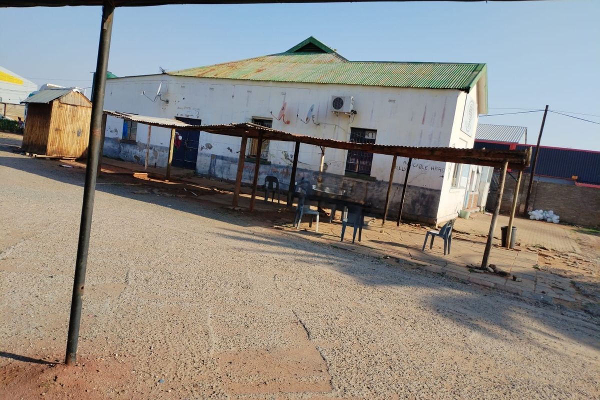 Front view of a commercial building featuring a corrugated metal roof, external air conditioning unit, and a covered outdoor walkway area.