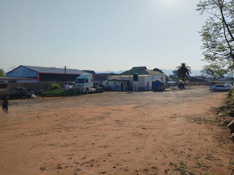A wide view of a commercial property featuring a large unpaved yard, a warehouse structure, and auxiliary buildings on the site.