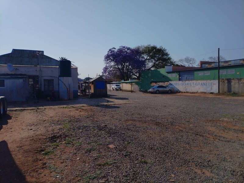 A commercial vacant land property featuring a gravel yard, perimeter wall, and an existing structure with a water storage tank.