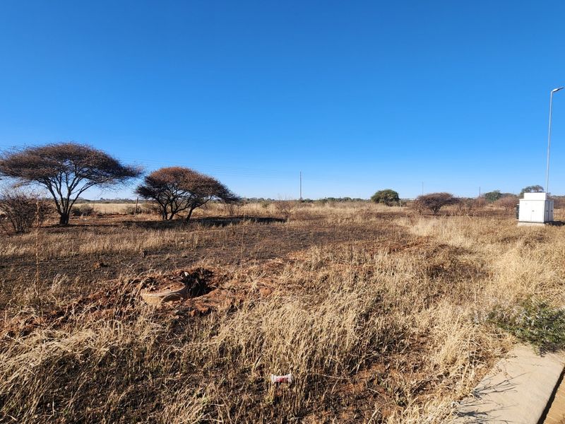 A vacant commercial land plot featuring dry vegetation, an electrical utility box, and street-side infrastructure access.