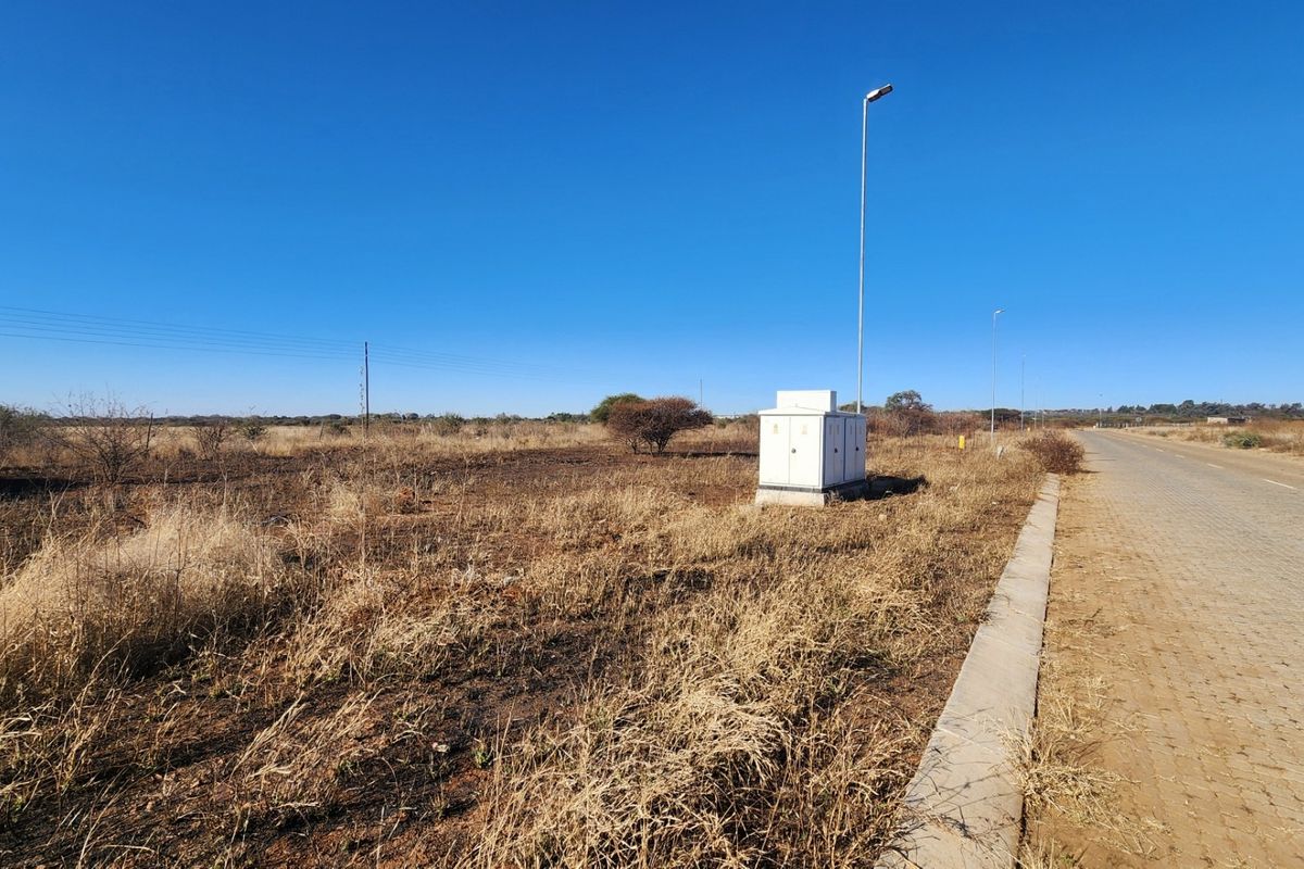 A view of a vacant commercial plot featuring a paved road, concrete curbing, and an existing electrical distribution box.