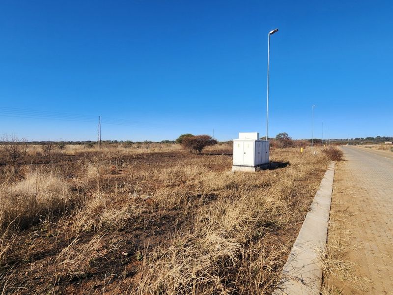 A view of a vacant commercial plot featuring a paved road, concrete curbing, and an existing electrical distribution box.