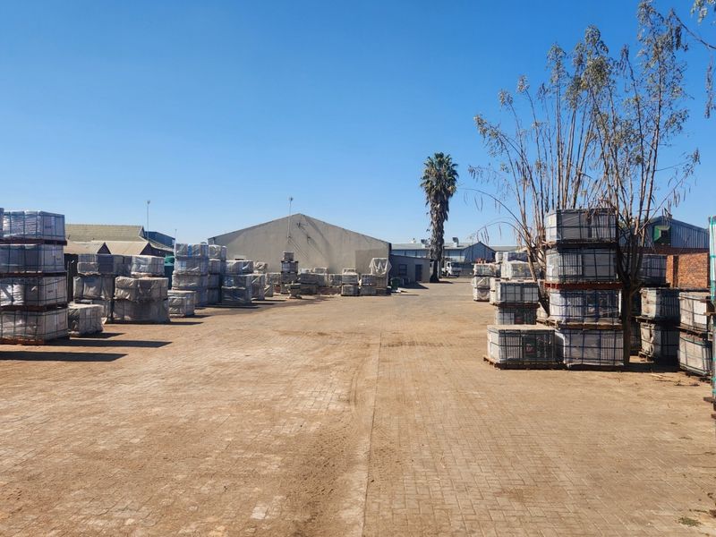 An expansive industrial yard featuring paved surfaces and large warehouse structures, currently utilized for bulk storage.