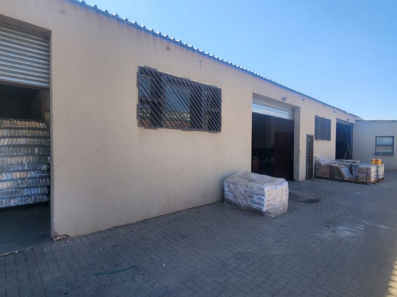 Industrial property exterior featuring multiple roller shutter access points, security-barred windows, and a paved yard area suitable for logistics or storage operations.