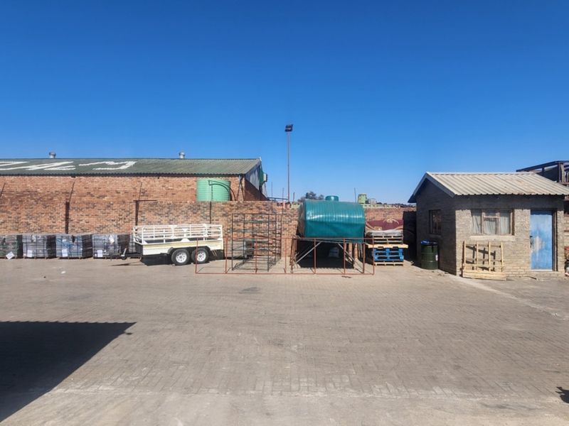 A spacious industrial yard featuring paved ground, brick perimeter walls, and a small utility structure with a corrugated metal roof.