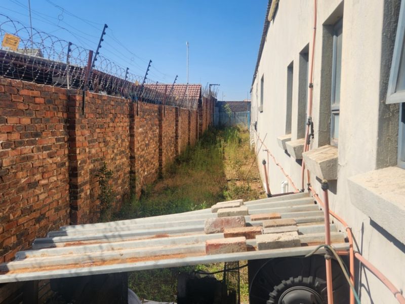 Rear exterior view of the industrial property featuring a brick boundary wall with security fencing and a weathered corrugated lean-to structure.