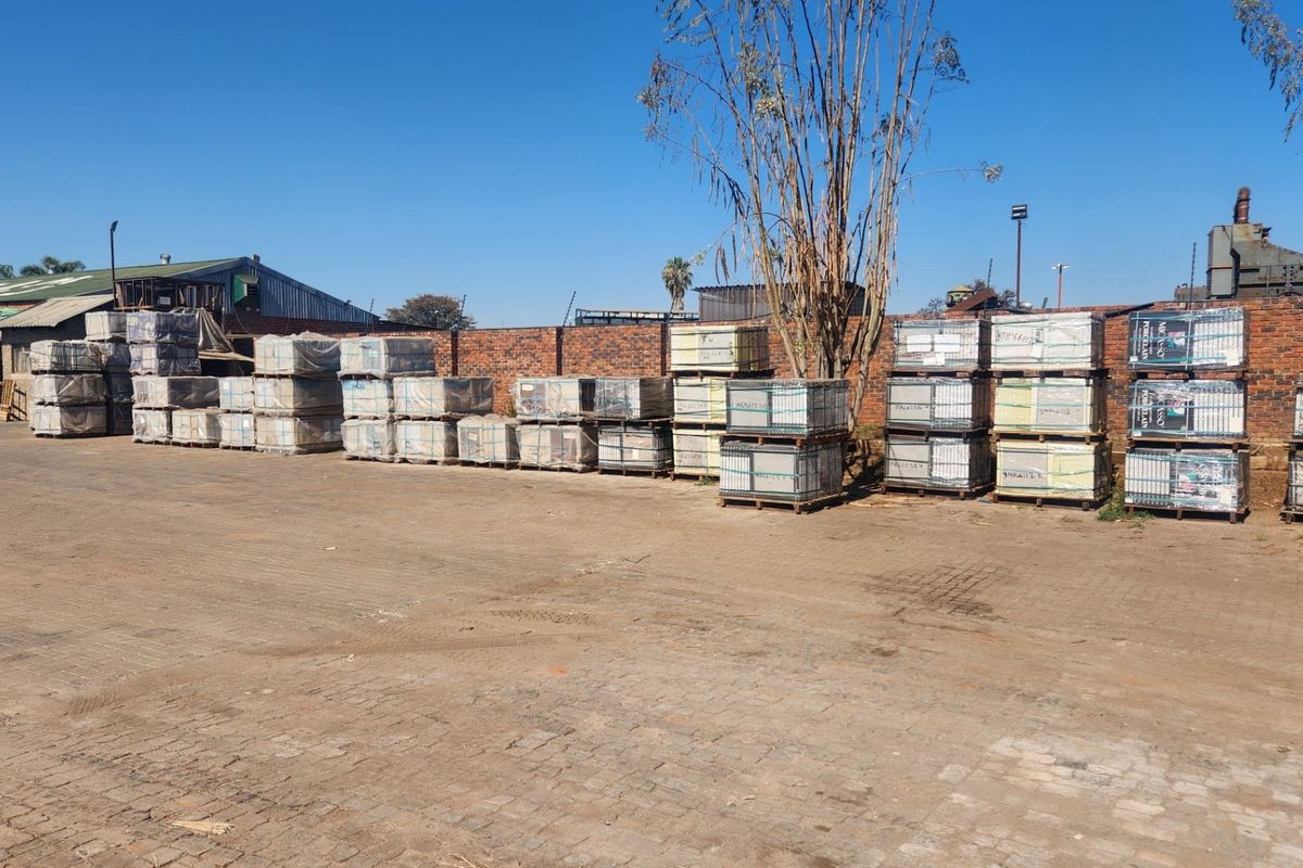 An industrial yard area featuring a paved surface, brick perimeter wall, and security fencing, suitable for storage or logistics operations.