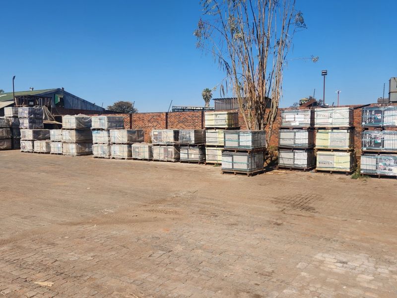 An industrial yard area featuring a paved surface, brick perimeter wall, and security fencing, suitable for storage or logistics operations.