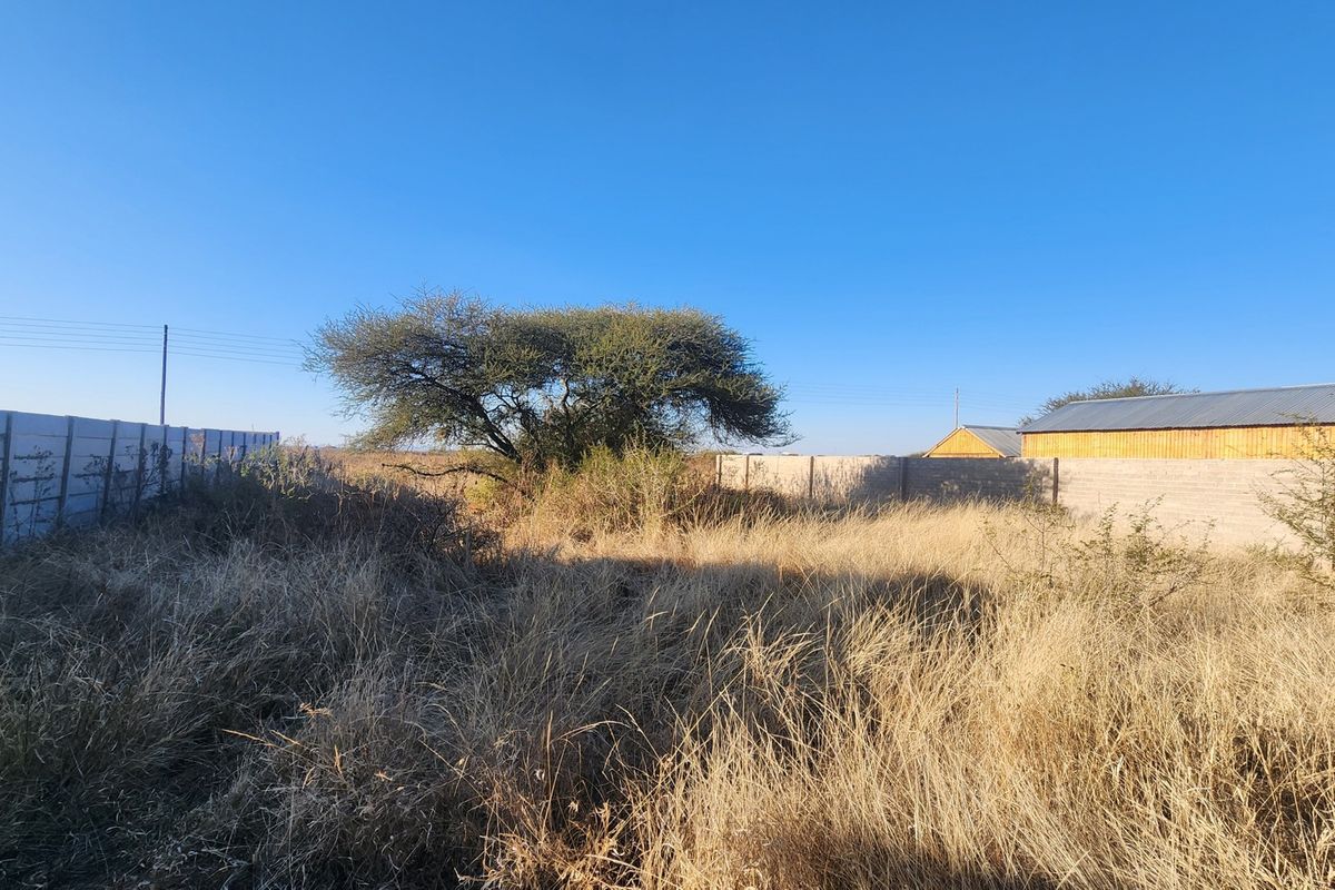 A vacant commercial plot featuring a precast concrete boundary wall and overgrown dry grass, offering a clear space for potential development.