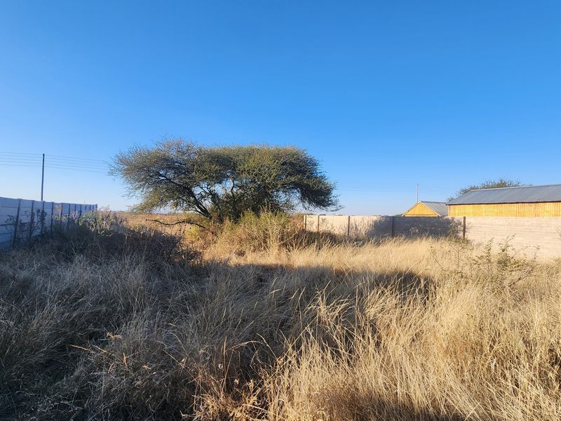 A vacant commercial plot featuring a precast concrete boundary wall and overgrown dry grass, offering a clear space for potential development.