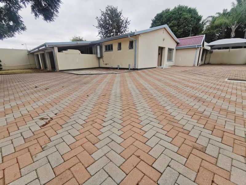 Spacious rear exterior area featuring extensive herringbone brick paving, perimeter walling, and functional guttering systems surrounding the office building structure.