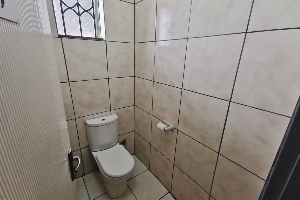 A compact, tiled office restroom featuring a standard toilet and a small window with a security grille.