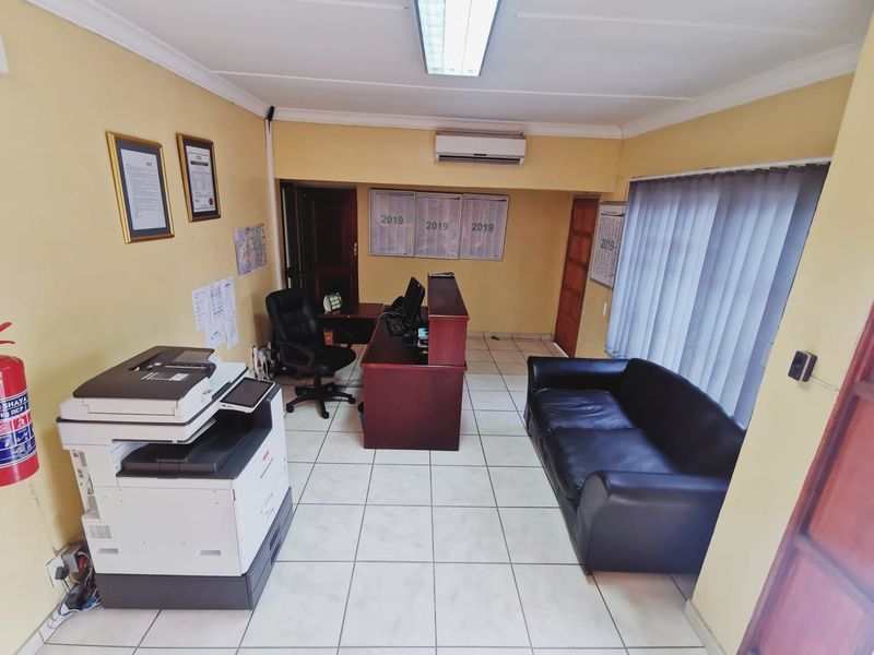 A functional office space featuring ceramic tiled flooring, a wall-mounted air conditioning unit, and vertical window blinds.