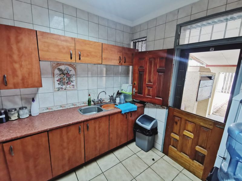 A functional kitchen area featuring built-in wooden cabinetry, laminate countertops, a stainless steel sink, and a stable door leading to an outdoor space.