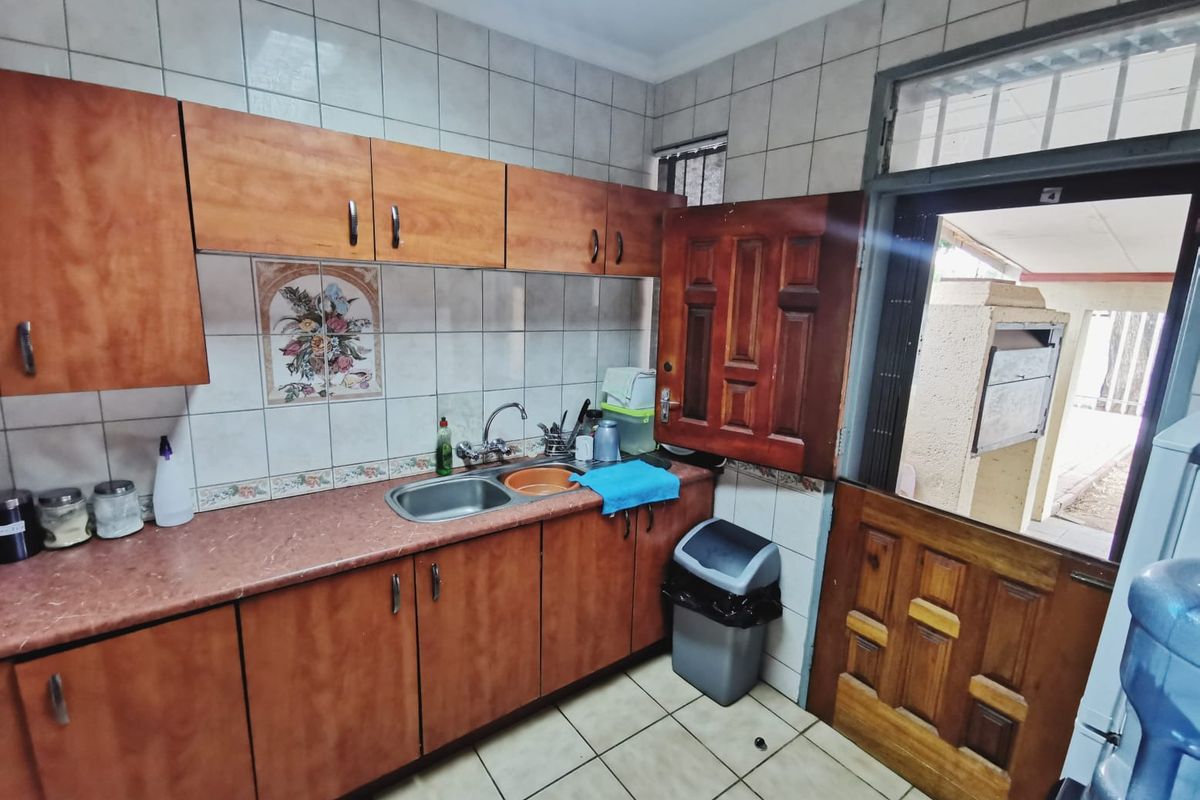 A functional kitchen area featuring built-in wooden cabinetry, laminate countertops, a stainless steel sink, and a stable door leading to an outdoor space.