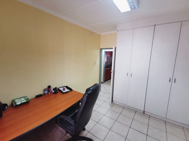 A functional office space featuring built-in storage cupboards, ceramic tiled flooring, and direct access to an adjacent room.