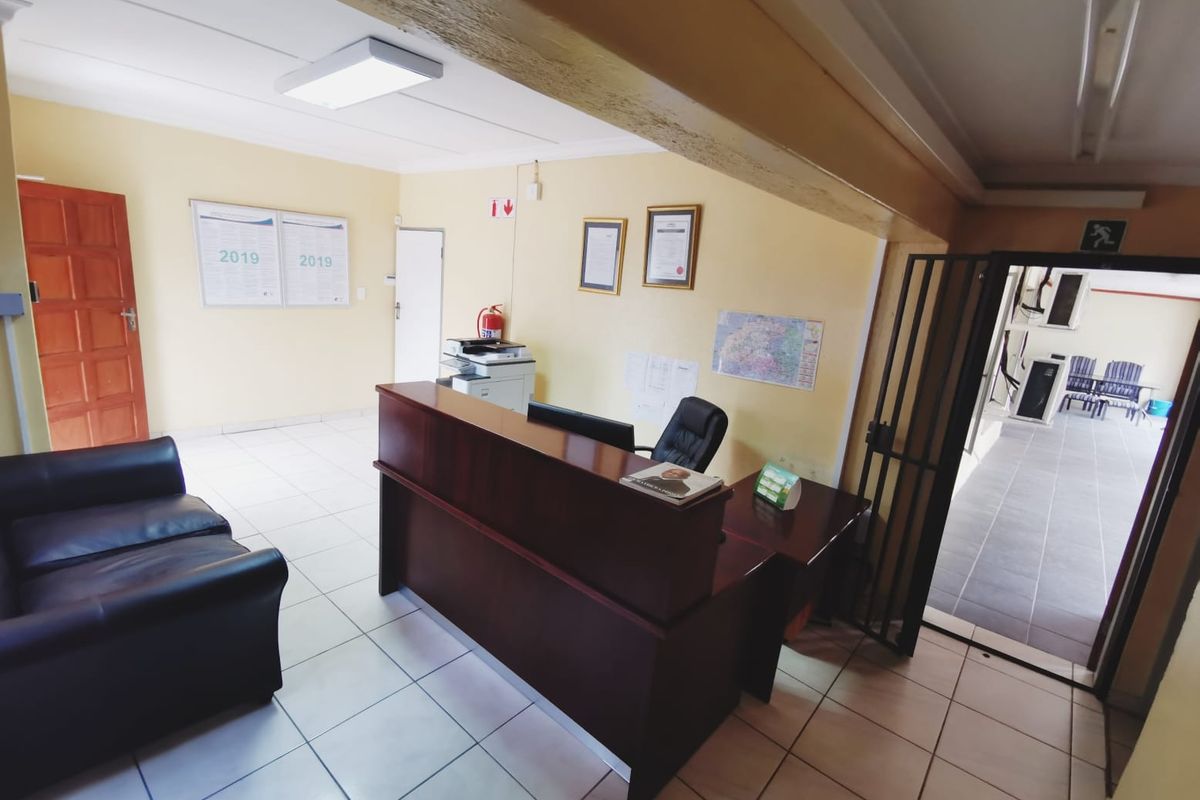 A functional office reception area featuring a built-in desk, tiled flooring, and a security gate leading to an outdoor walkway.