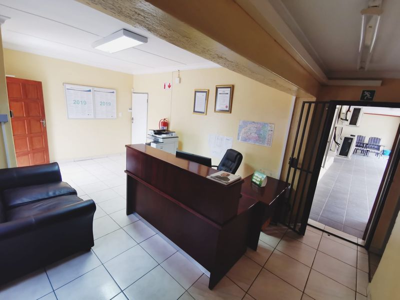 A functional office reception area featuring a built-in desk, tiled flooring, and a security gate leading to an outdoor walkway.