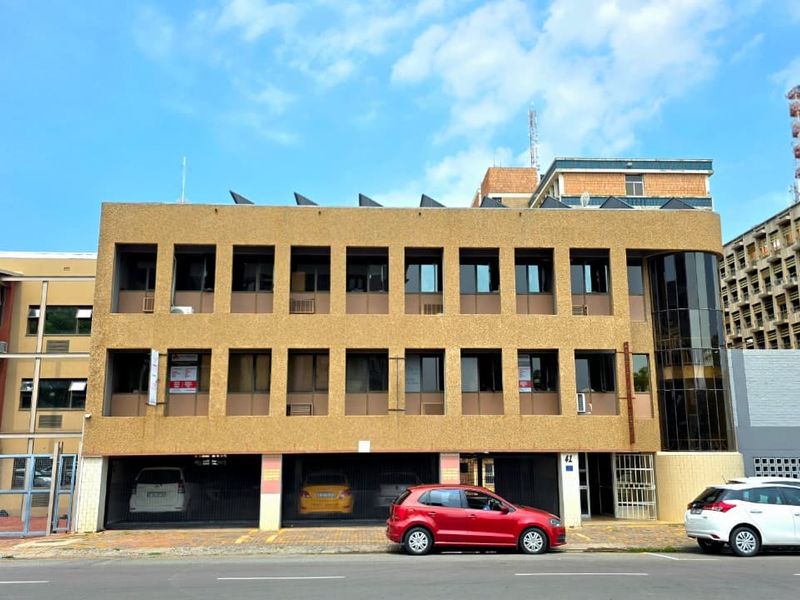 Front elevation of a multi-story commercial office building featuring a textured facade, integrated ground-level covered parking, and modern glass curtain wall detailing.
