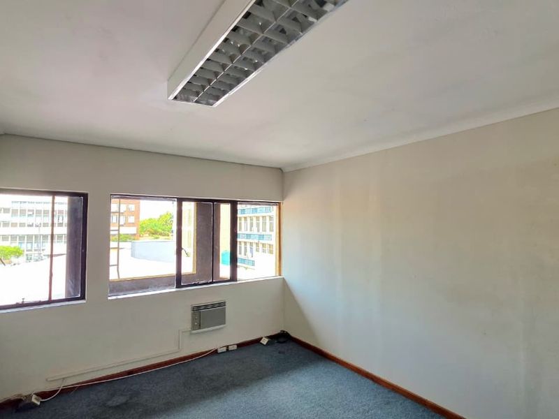 An empty office space featuring carpet flooring, a built-in window air conditioning unit, and a fluorescent ceiling light fixture.