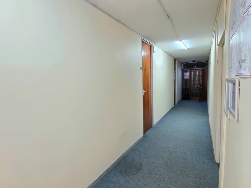 A functional office hallway featuring carpeted flooring, fluorescent lighting, and multiple wooden access doors.