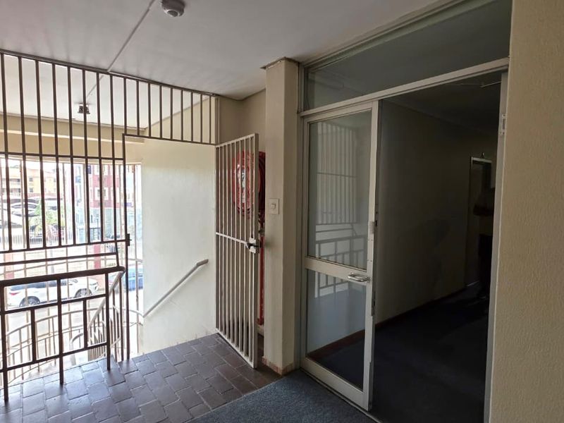 An office building entry area featuring a security gate, fire safety equipment, and a glass door leading into the interior hallway.