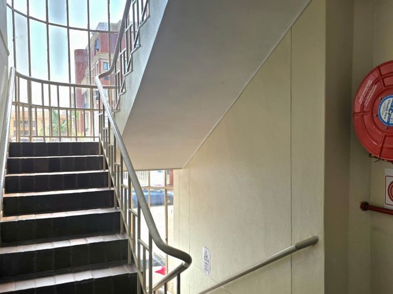 A functional office building stairwell featuring a metal handrail, tiled steps, and a wall-mounted fire hose reel for safety compliance.