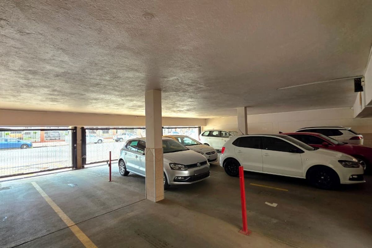 Covered parking garage area featuring concrete flooring, support columns, and secure metal gate access.