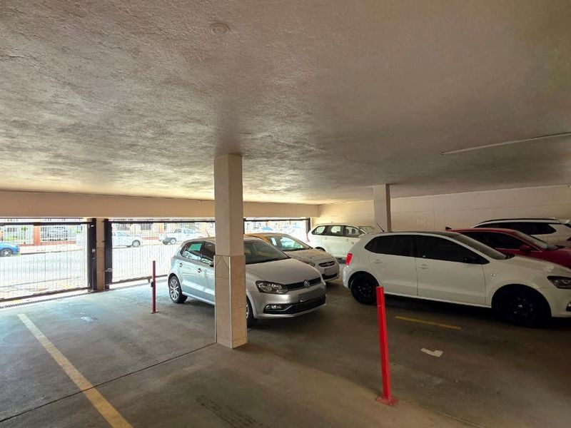 Covered parking garage area featuring concrete flooring, support columns, and secure metal gate access.