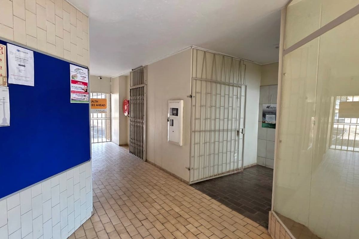 A functional office hallway featuring tiled flooring, security gates, and glass partitions, providing access to various office units.