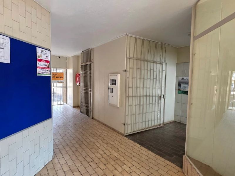 A functional office hallway featuring tiled flooring, security gates, and glass partitions, providing access to various office units.