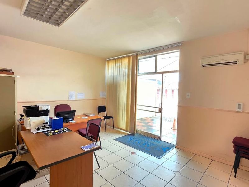 A functional office space featuring tiled flooring, a split-system air conditioner, and direct access to an outdoor area through a glass panel door.