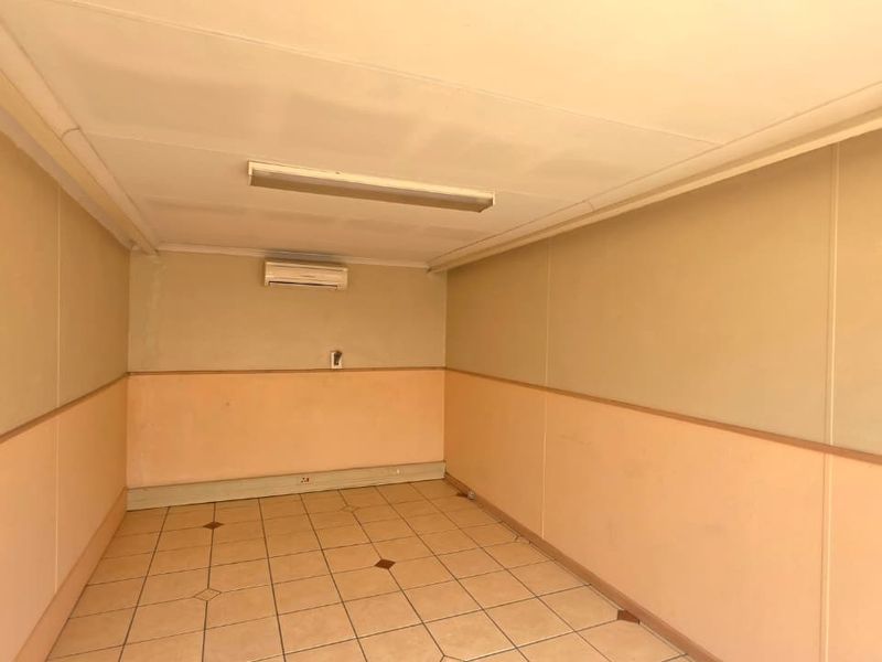 A vacant office space featuring tiled flooring, a wall-mounted air conditioning unit, and fluorescent lighting, ready for customization or professional fit-out.