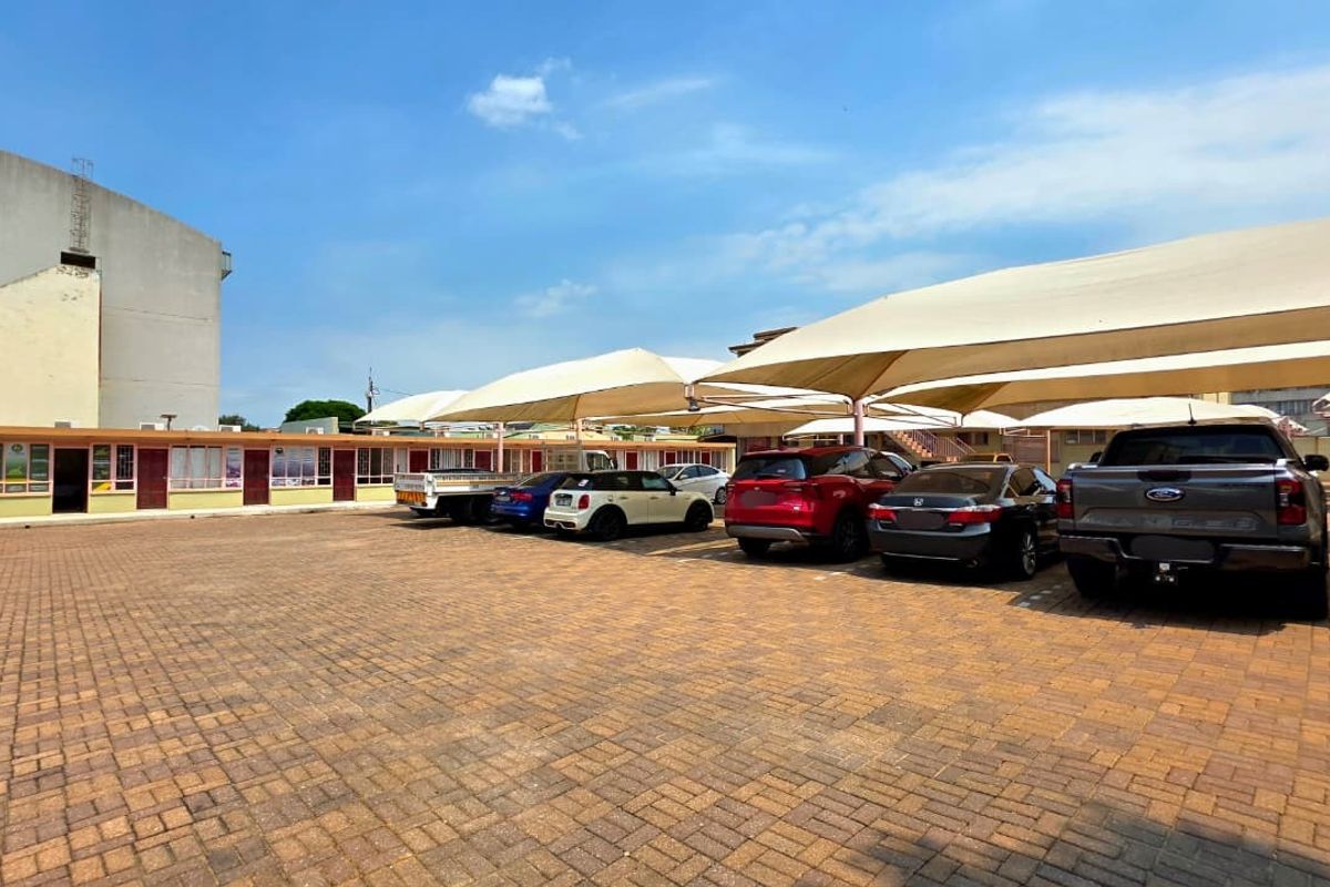 A paved parking area featuring multiple shade cloth carports serving a single-story office building.