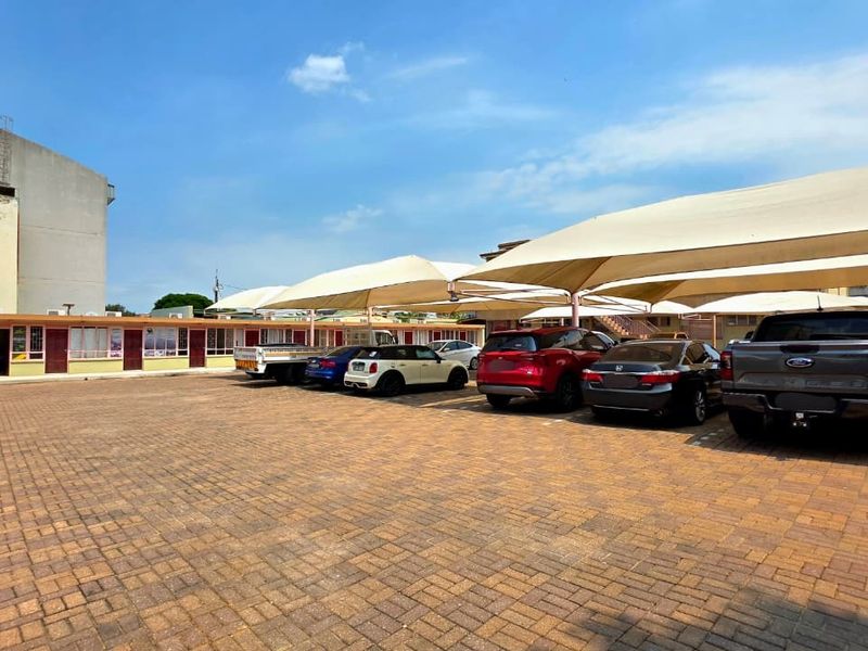 A paved parking area featuring multiple shade cloth carports serving a single-story office building.