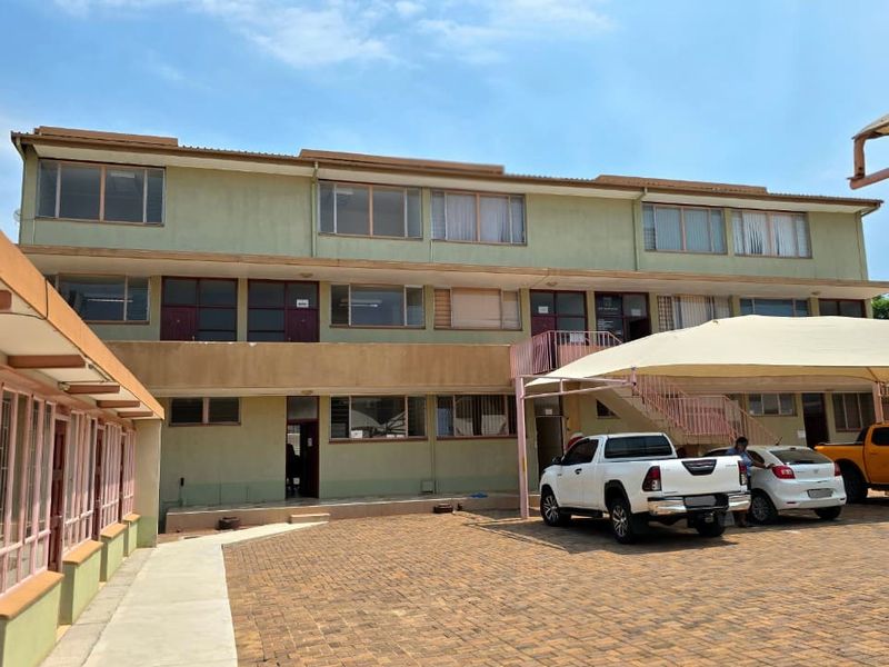 A multi-story office building exterior featuring a paved parking area with shade cloth carports and functional aluminum window frames.