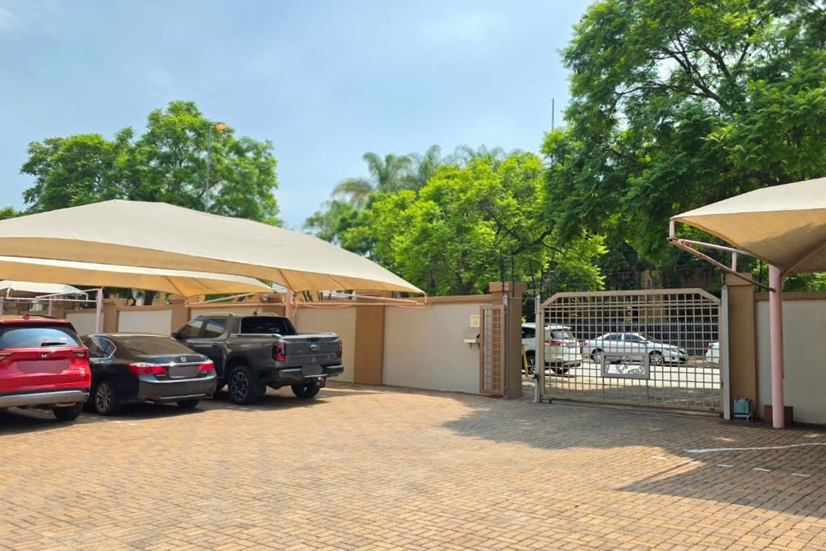A paved office parking area featuring secure perimeter walls, a gated entrance, and multiple shade cloth carports for vehicle protection.