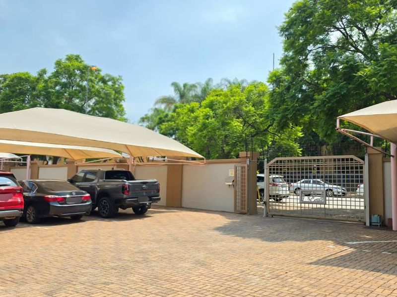 A paved office parking area featuring secure perimeter walls, a gated entrance, and multiple shade cloth carports for vehicle protection.