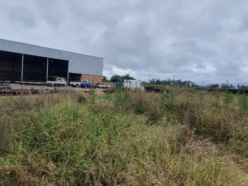 Vacant commercial land featuring an existing metal warehouse structure and perimeter fencing, currently covered in overgrown vegetation.