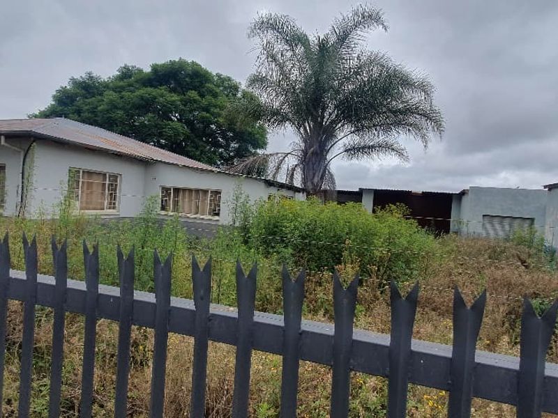 Street view of a commercial property featuring multiple structures, metal fencing, and significant overgrown vegetation requiring site clearance and maintenance.
